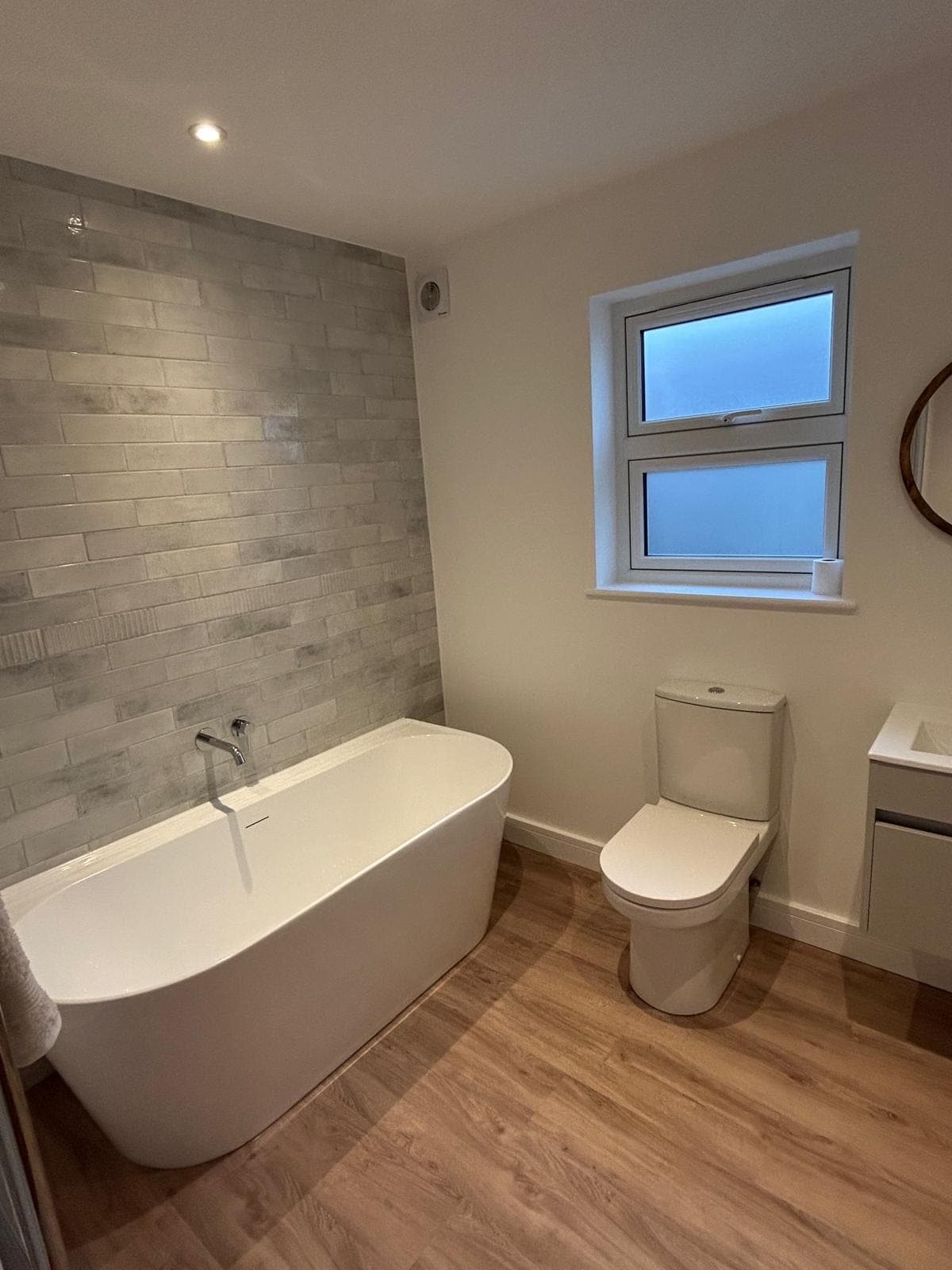Renovated family bathroom with a freestanding bath, feature tiled wall and oak-effect flooring