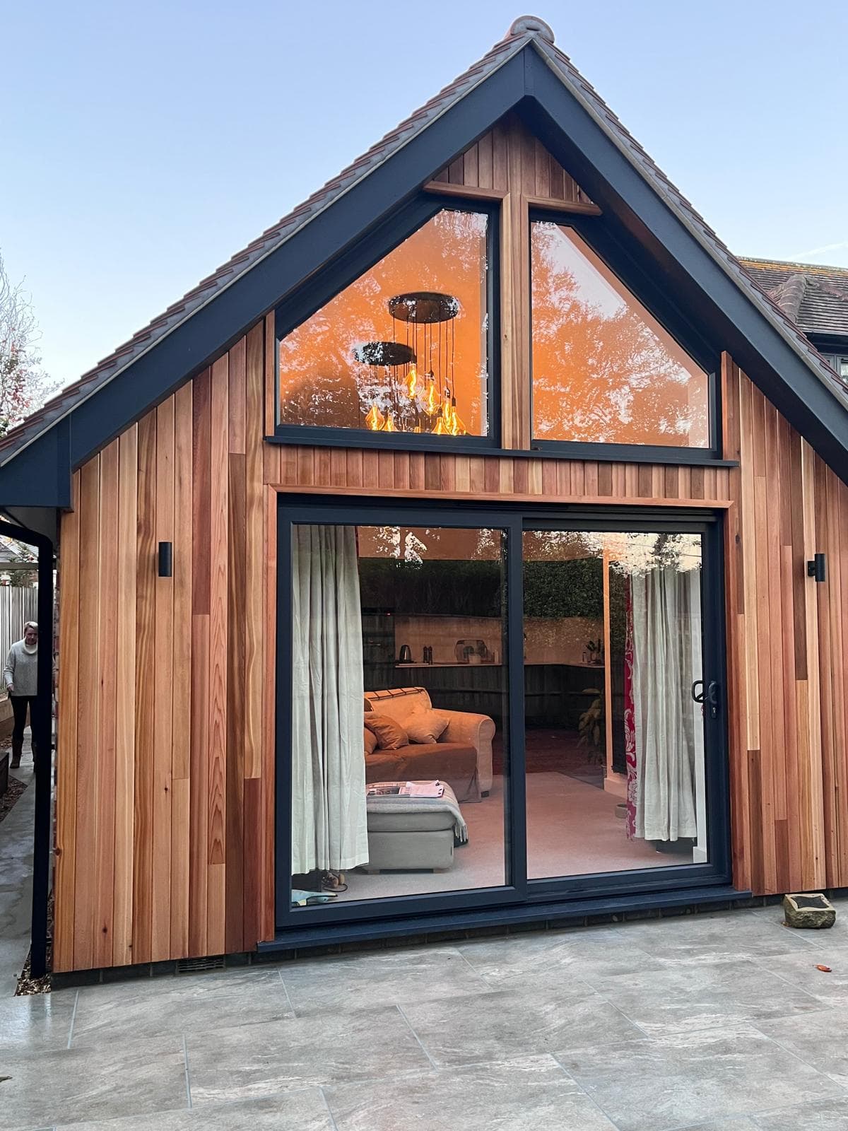 Cedar-clad garden room with an oak-framed apex glazed gable, glowing at dusk, crafted by FR Carpentry