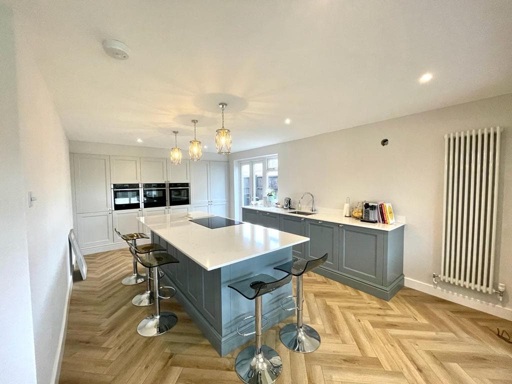 Grey shaker kitchen with a quartz-topped island, pendant lights and herringbone oak flooring